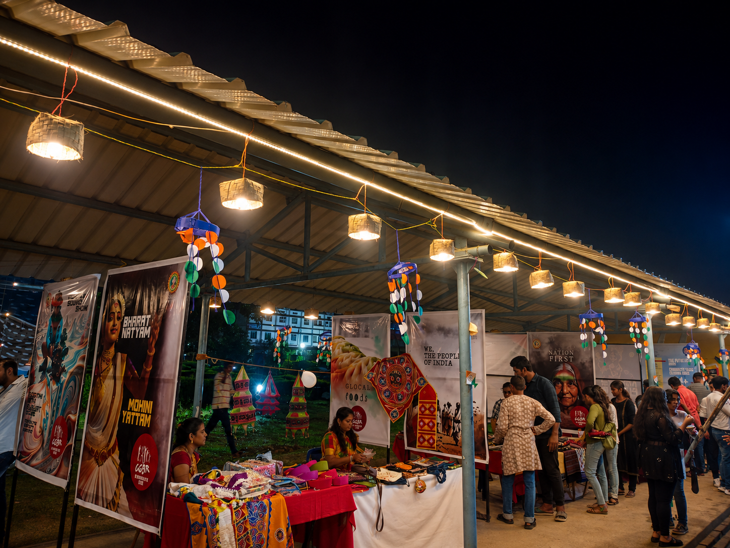 Hands at work — a craft and cultural fair stall under a lit roof, with people gathered around tables of textiles and posters
